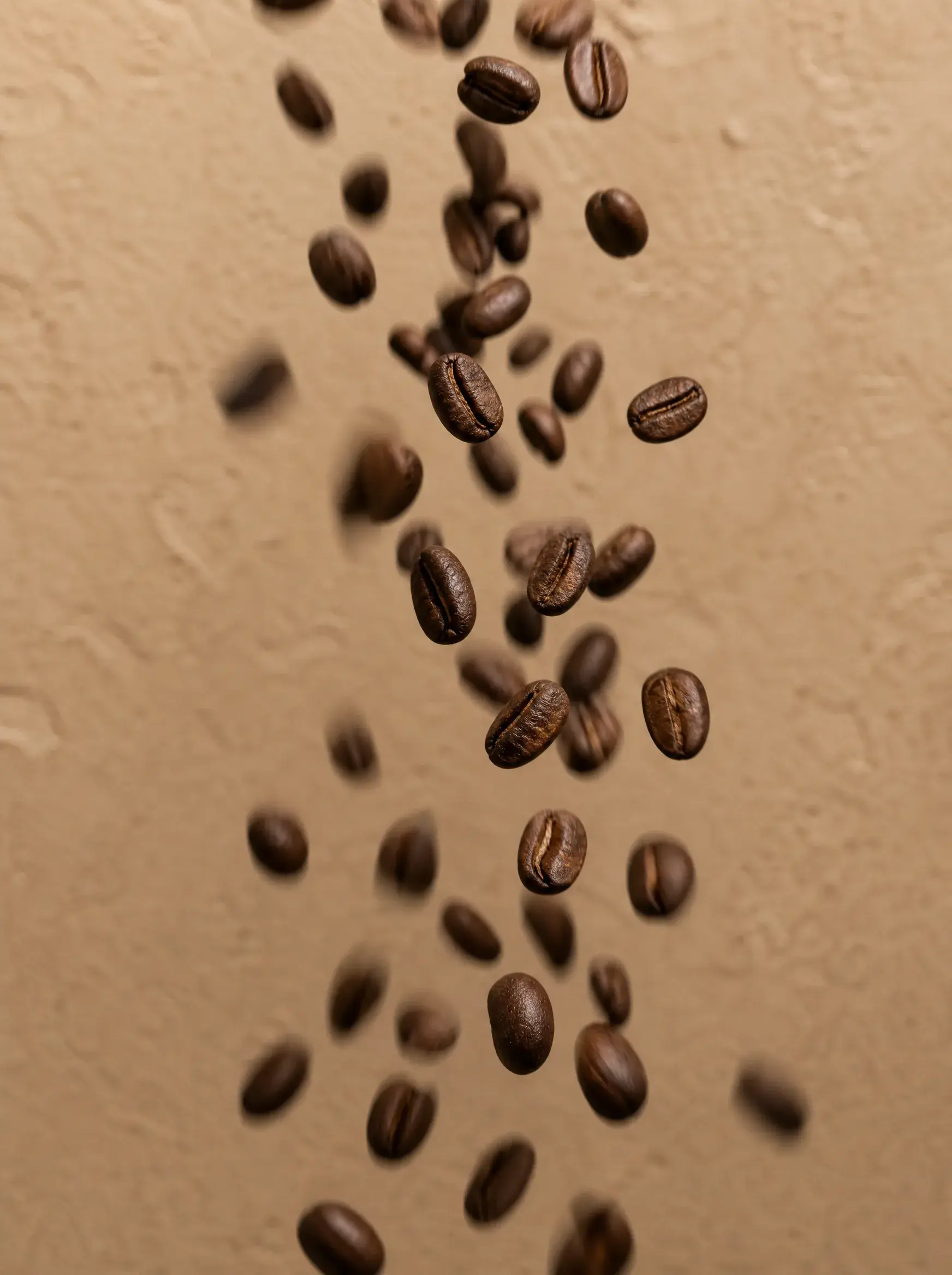 Grains de café torréfiés en chute libre – mouvement, cascade, fond beige texturé
