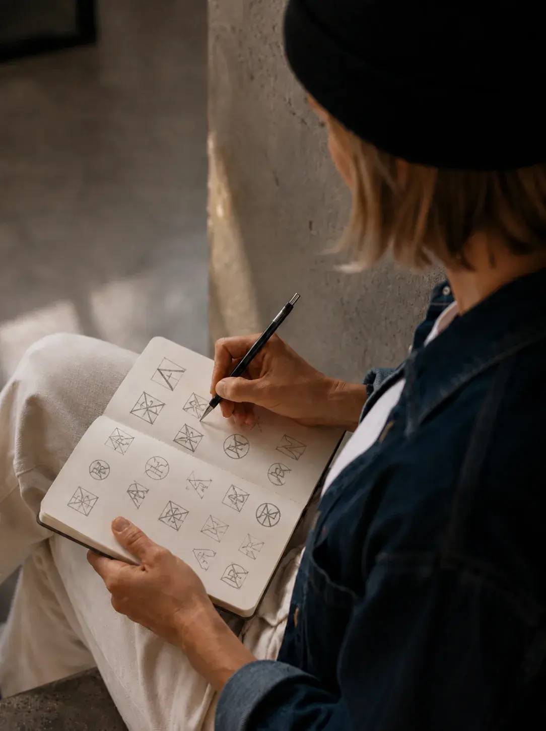 Graphiste assise dessinant des esquisses de logos géométriques triangulaires dans un carnet de croquis, bonnet noir