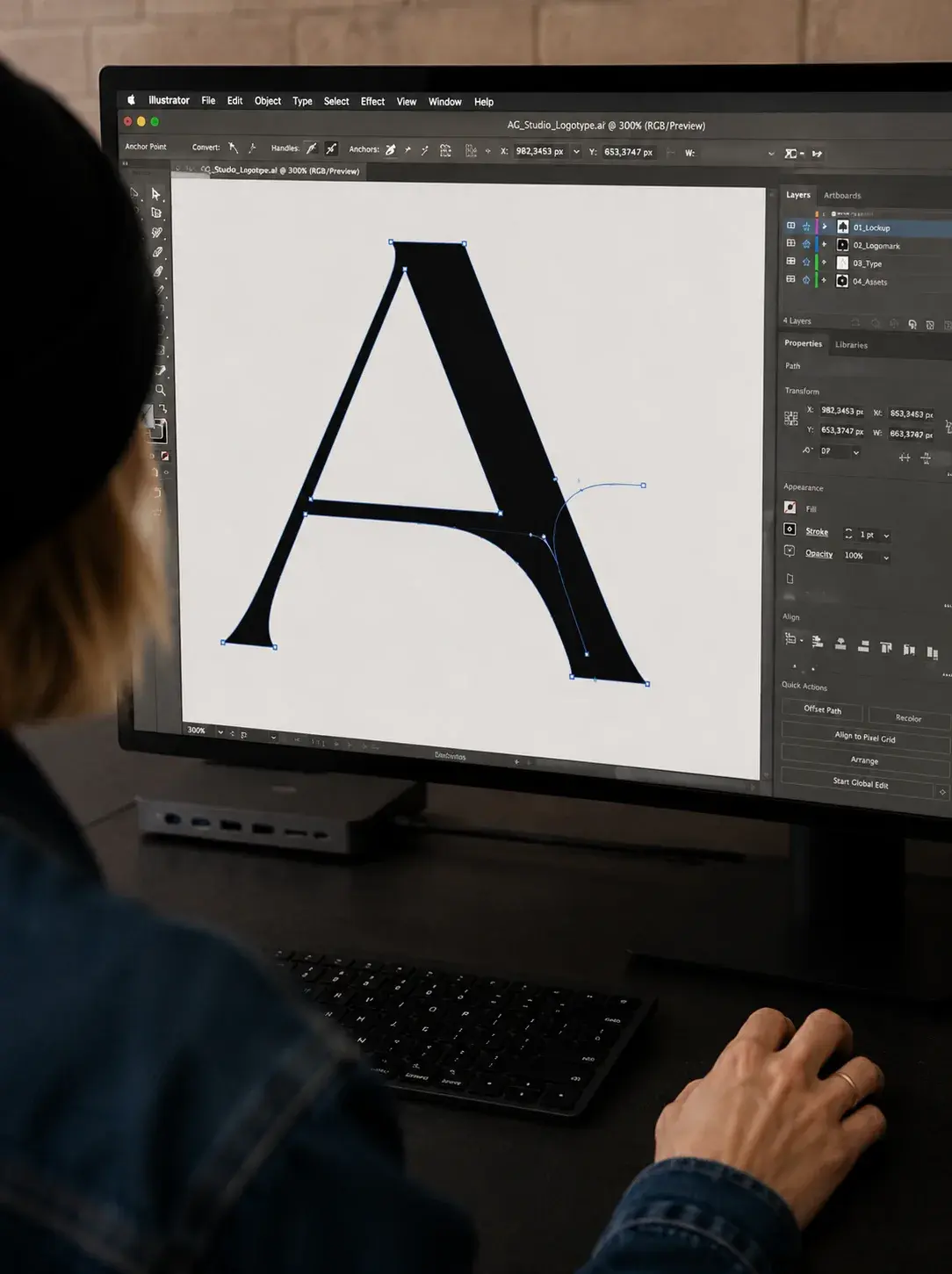 Graphiste de dos travaillant sur la construction d'une grande lettre A serif dans Adobe Illustrator sur écran large