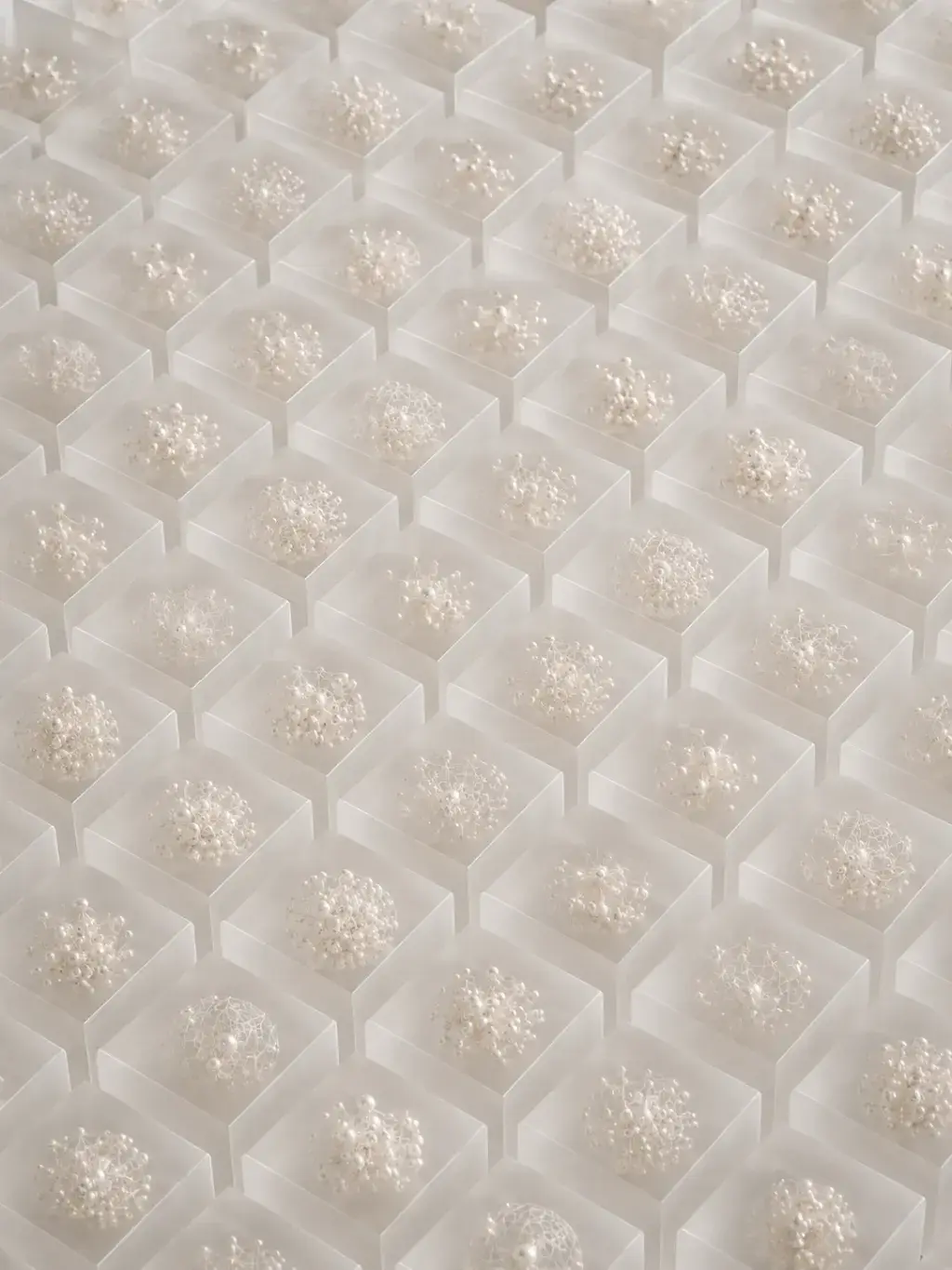 Grille de cubes en résine givrée contenant chacun un agrégat de perles, vue plongeante
