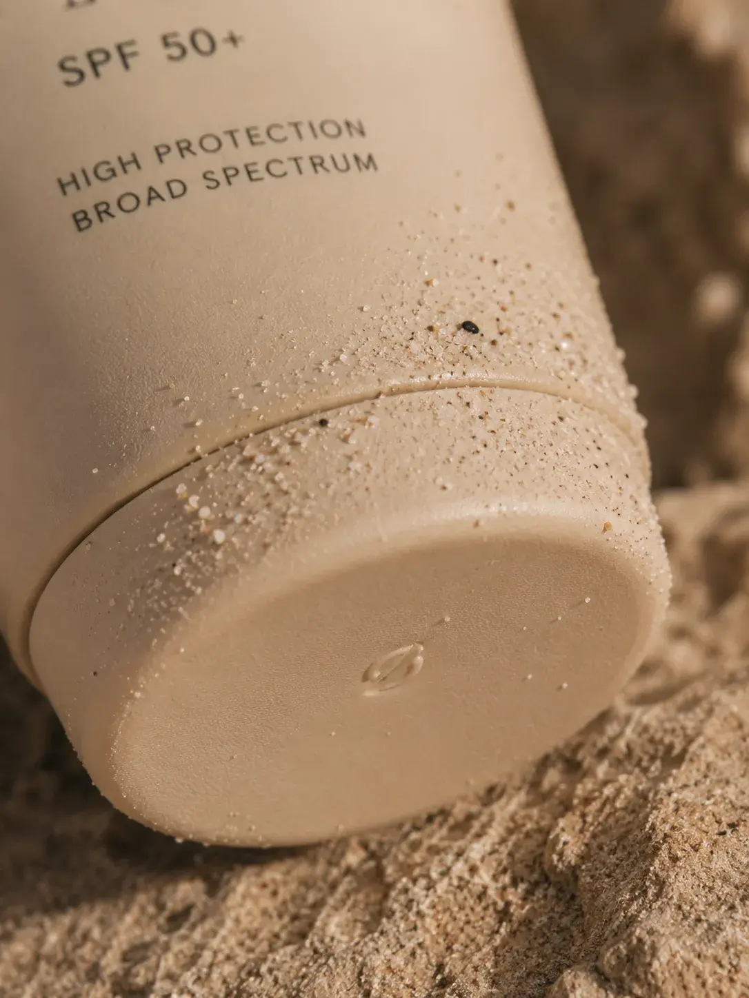 Gros plan base de tube crème solaire couvert de sable – SPF 50+, plage, texture granuleuse