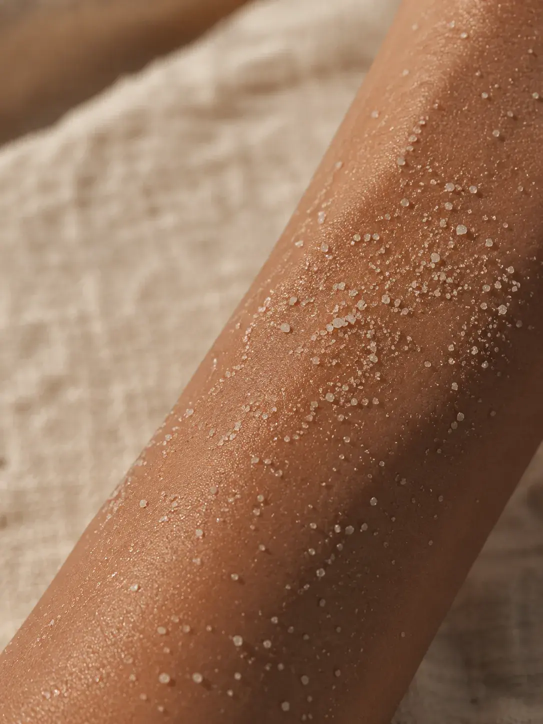 Gros plan bras bronzé avec gommage sel marin – grains exfoliant blancs sur peau, fond lin
