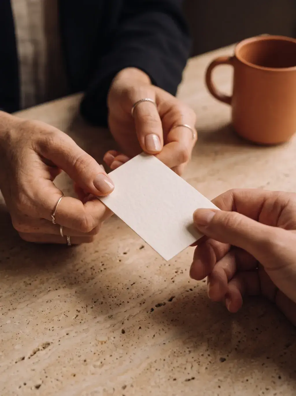 Gros plan de deux mains échangeant une carte de visite blanche sur une table en marbre