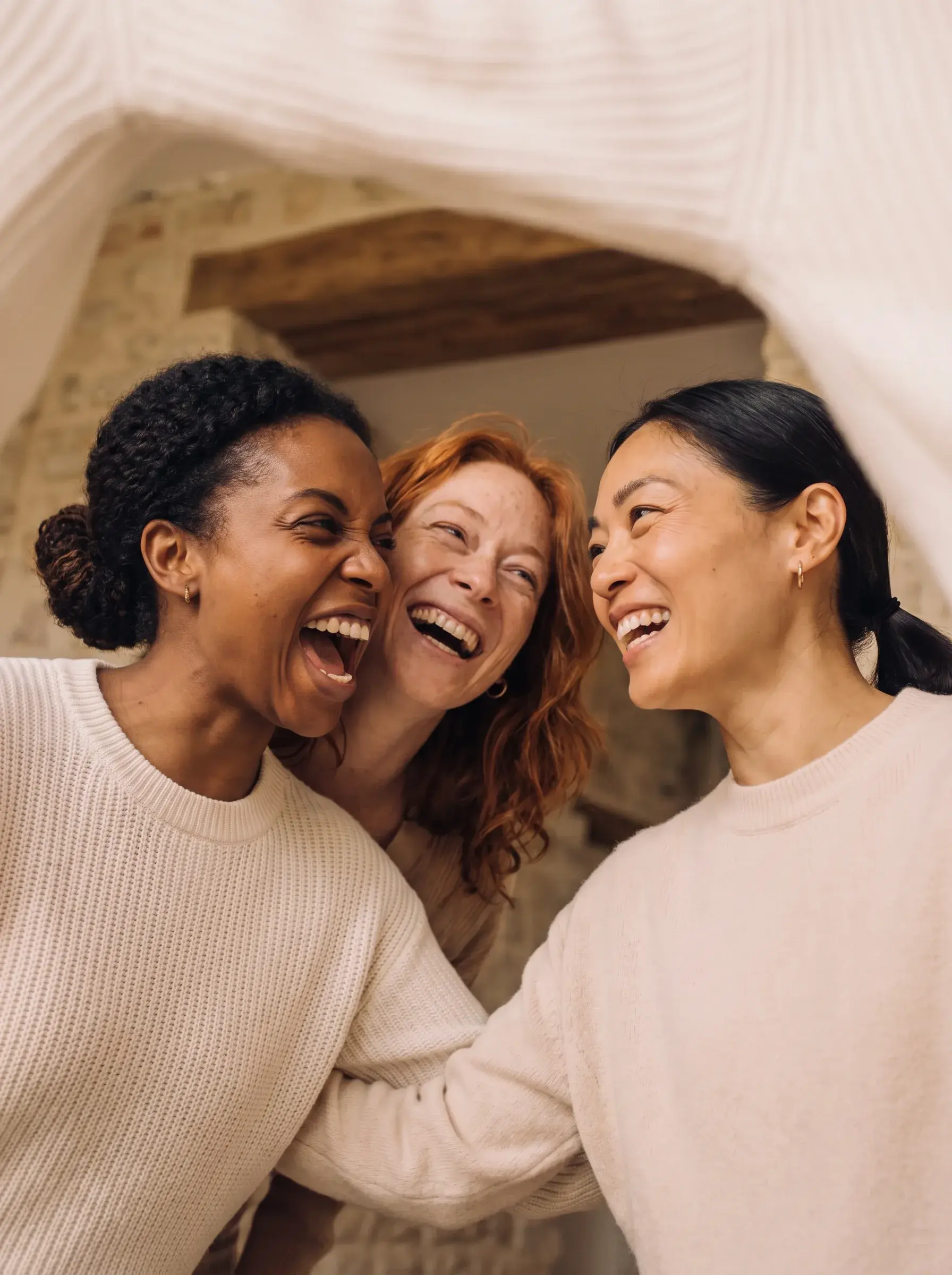 Gros plan de trois femmes de trois origines différentes riant ensemble sous un voile blanc