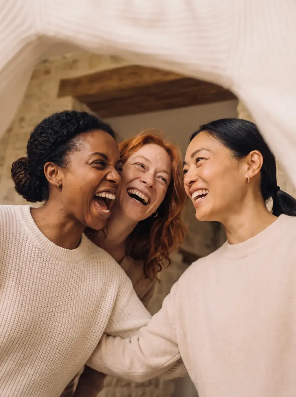 Gros plan de trois femmes de trois origines différentes riant ensemble sous un voile blanc