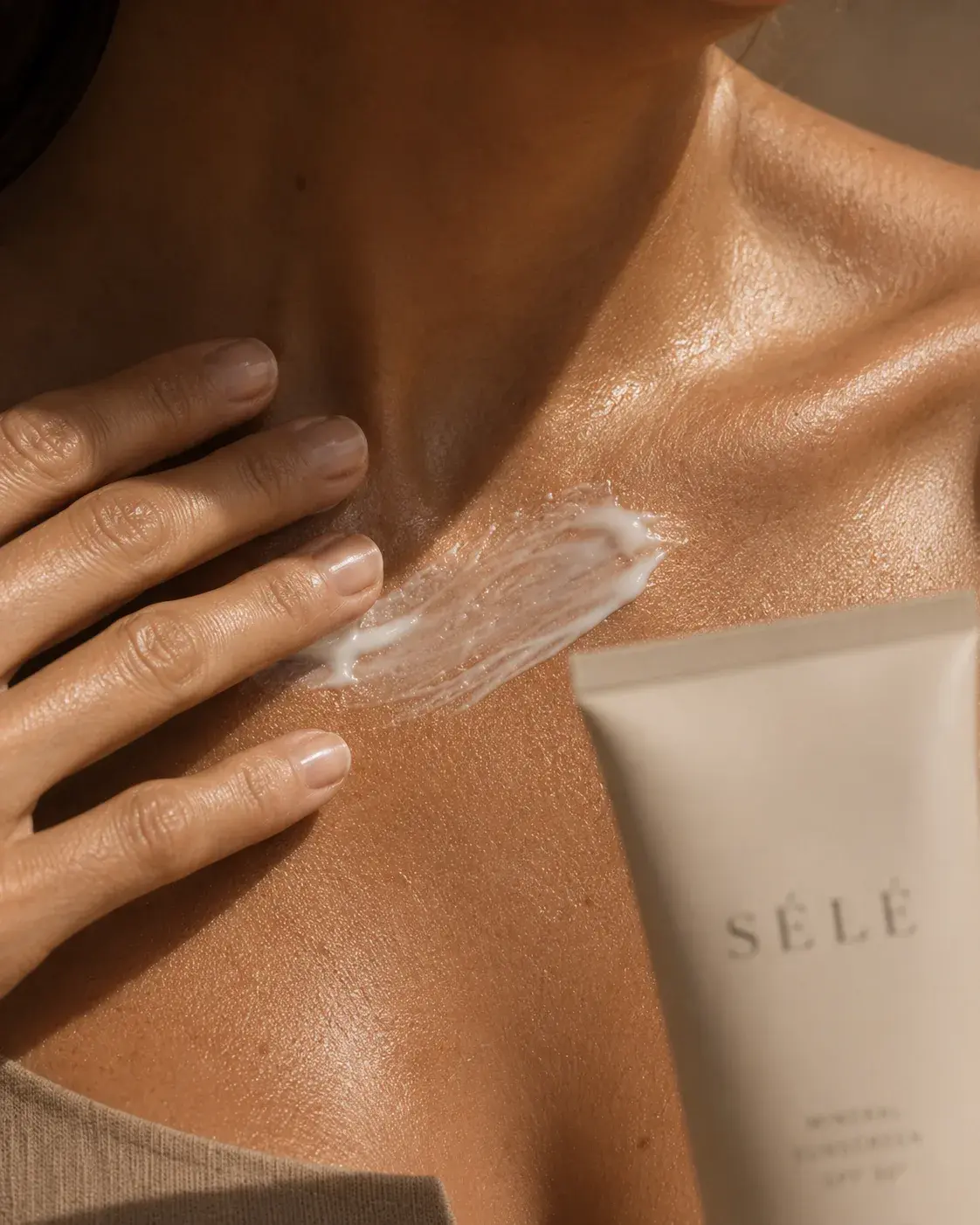 Gros plan décolleté peau bronzée – application crème blanche, tube cosmétique, lumière sombre