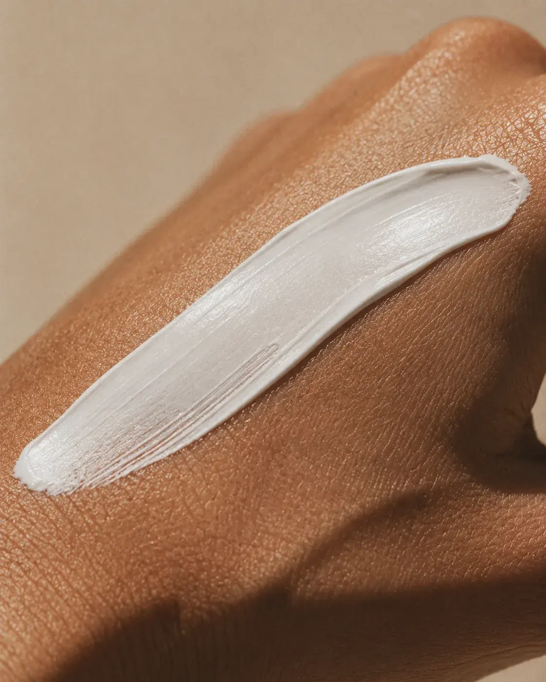 Gros plan dos de main peau noire – trace de crème blanche, swatch cosmétique, fond beige neutre