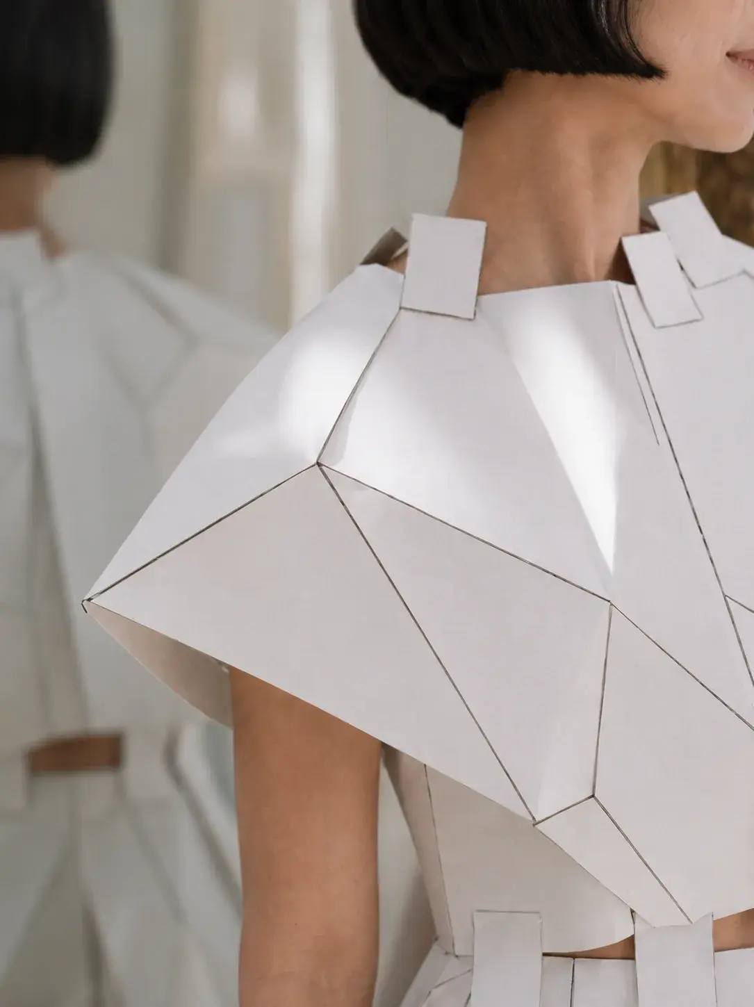 Gros plan dos et épaule en top origami géométrique – détail texture, deux mannequins
