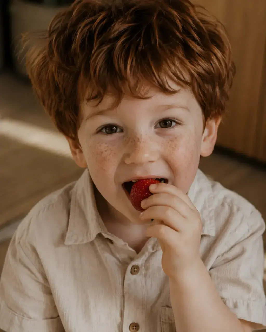 Gros plan enfant roux aux taches de rousseur mangeant une fraise – portrait spontané