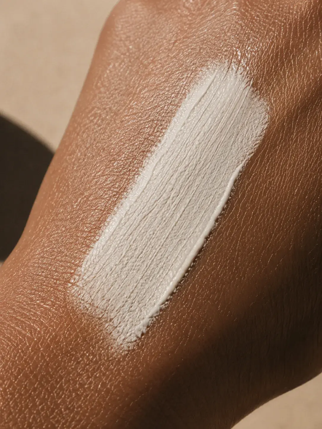 Gros plan main peau noire – trace de crème blanche, ombre marquée, fond sable lumineux