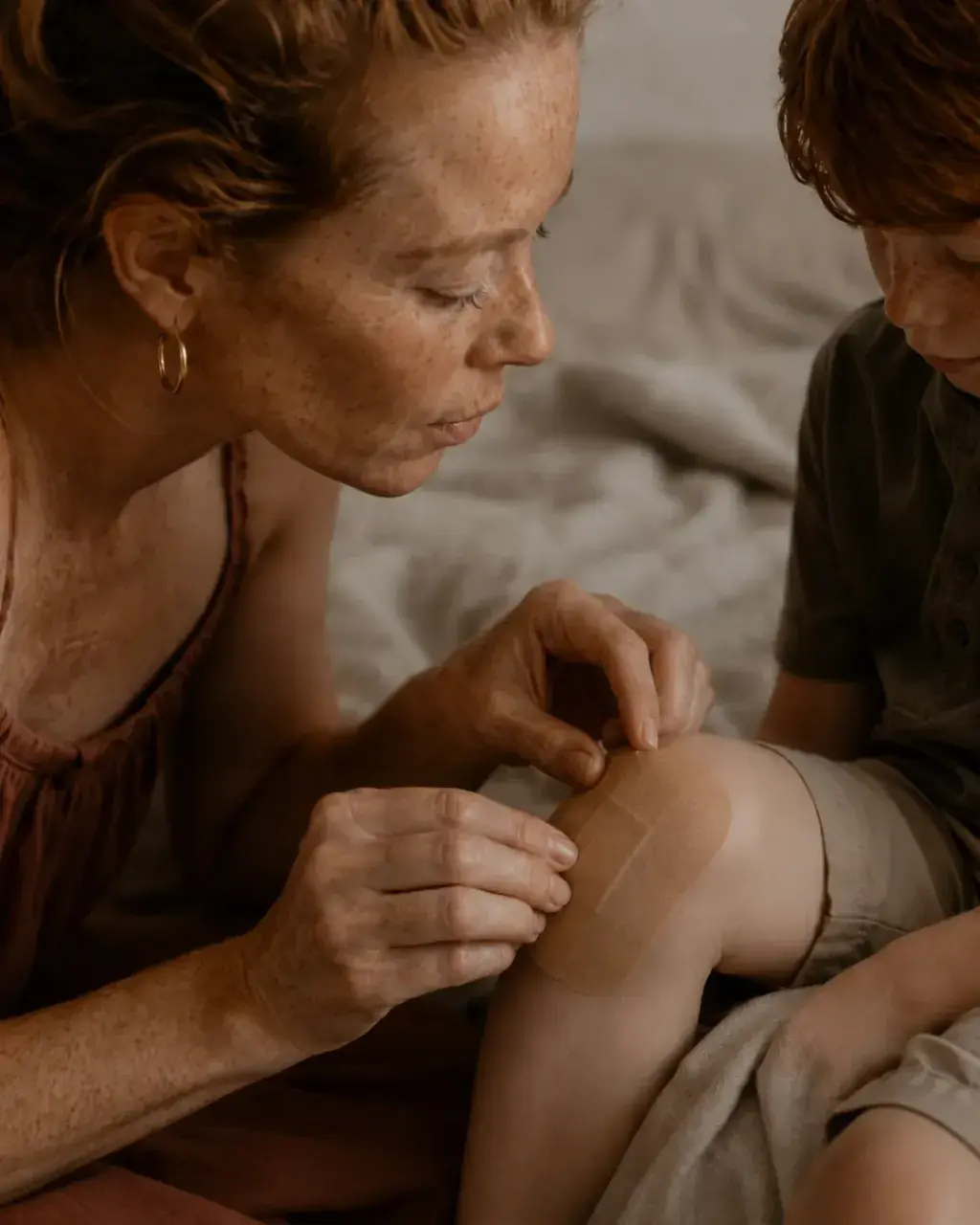Gros plan mère soignant un genou blessé – mains attentionnées, pansement et robe terracotta