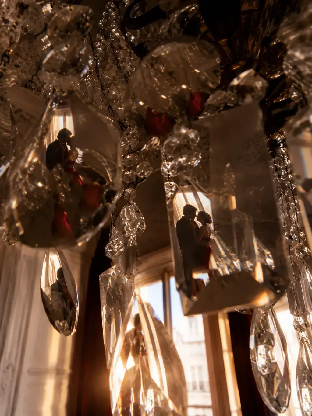 Gros plan sur pendeloques de cristal d'un lustre baroque avec reflets miniatures de couple s'embrassant et de cerises rouges