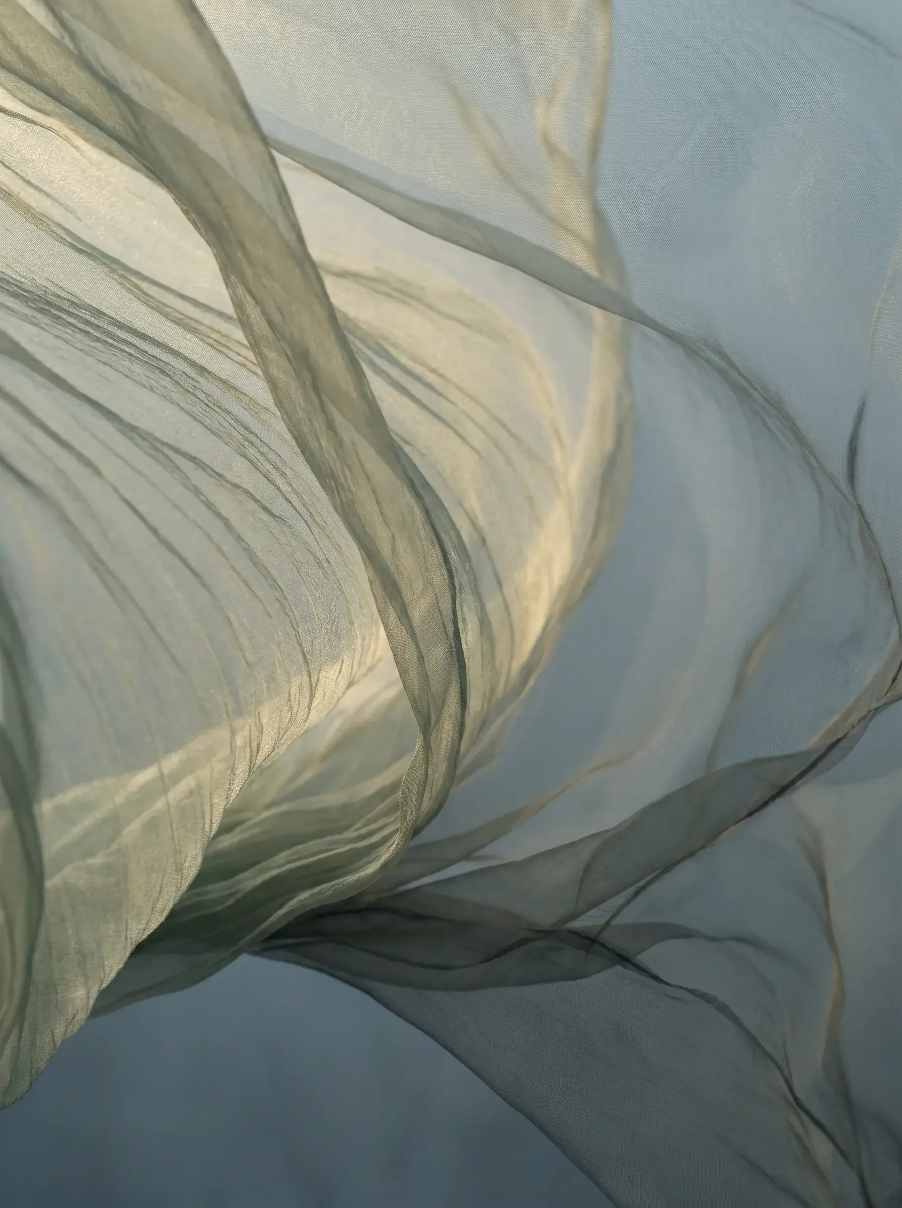 Gros plan texture voile gaze vert-doré – courbes et plis du tissu translucide, fond gris-bleu