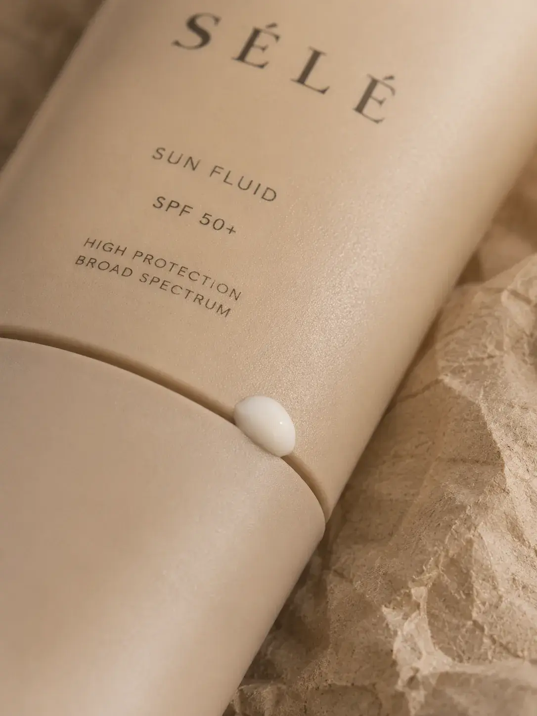 Gros plan tube fluide solaire – perle de crème blanche sortant du bouchon, fond kraft froissé