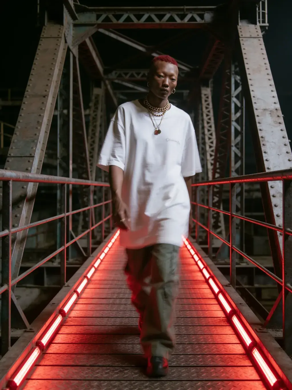 Homme aux cheveux rouges marchant vers l'objectif sur une passerelle industrielle aux rails LED rouges