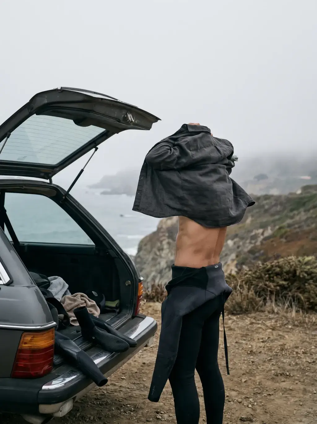 Homme de dos se changeant au bord d'une falaise côtière près d'un break de vague