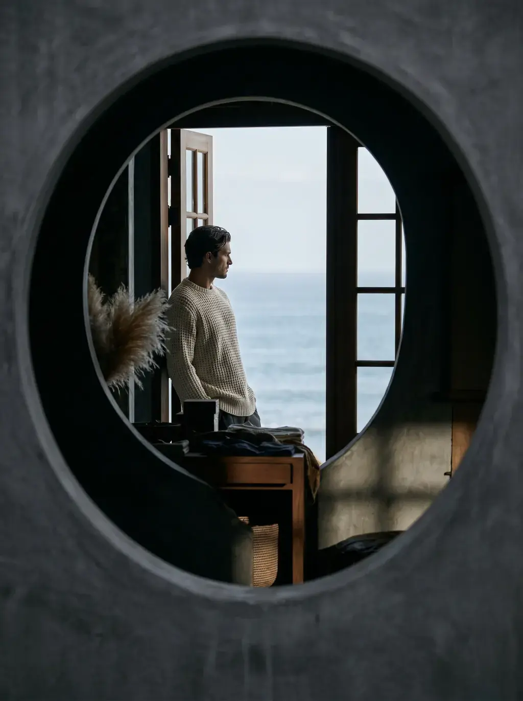 Homme en pull blanc visible à travers un hublot rond avec vue sur la mer