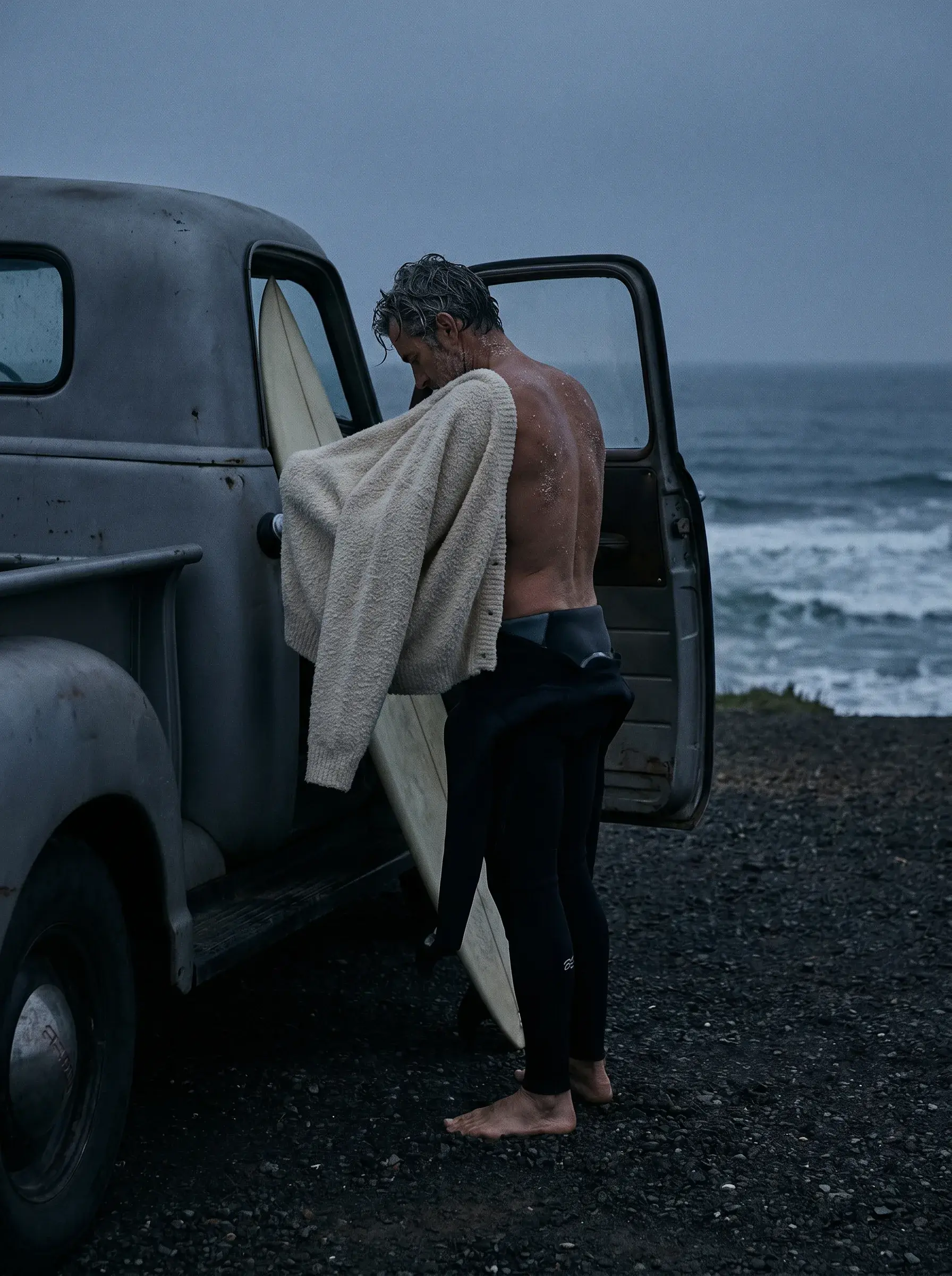 Homme mûr avec plaid sur l'épaule appuyé contre une camionnette vintage en bord de mer