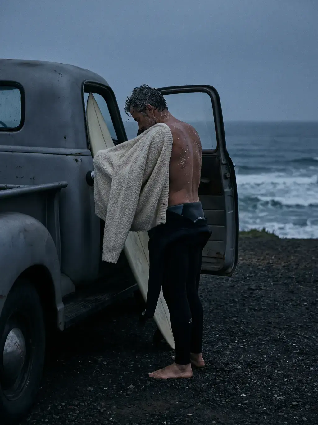 Homme mûr avec plaid sur l'épaule appuyé contre une camionnette vintage en bord de mer