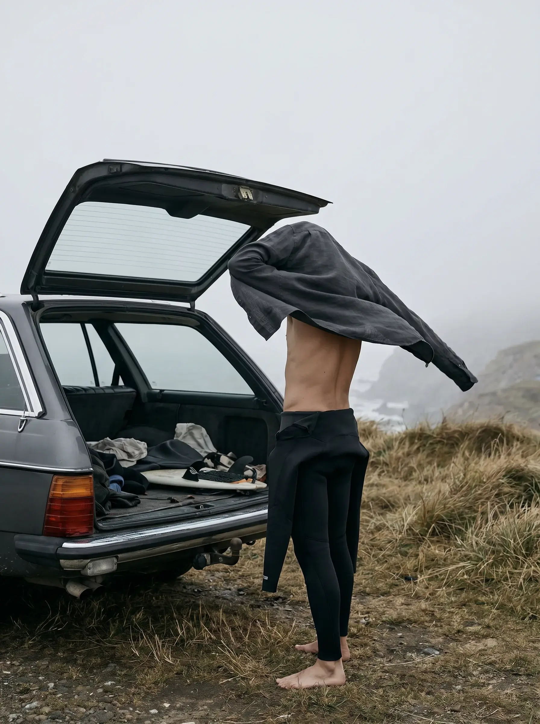 Homme retirant sa veste mouillée près d'une voiture vintage sur une falaise côtière