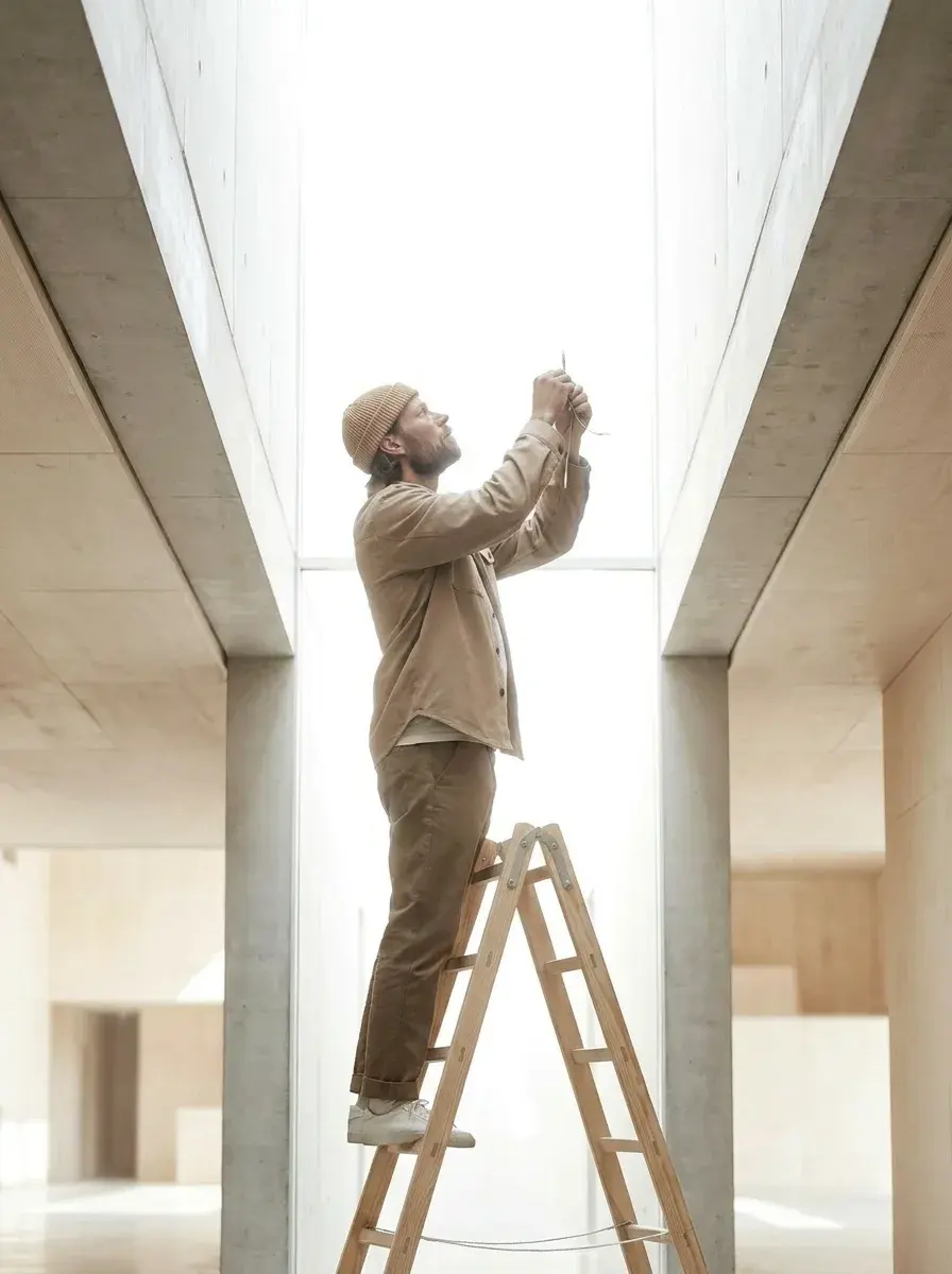 Homme sur un escabeau installant un éclairage dans une faille lumineuse entre deux murs en béton