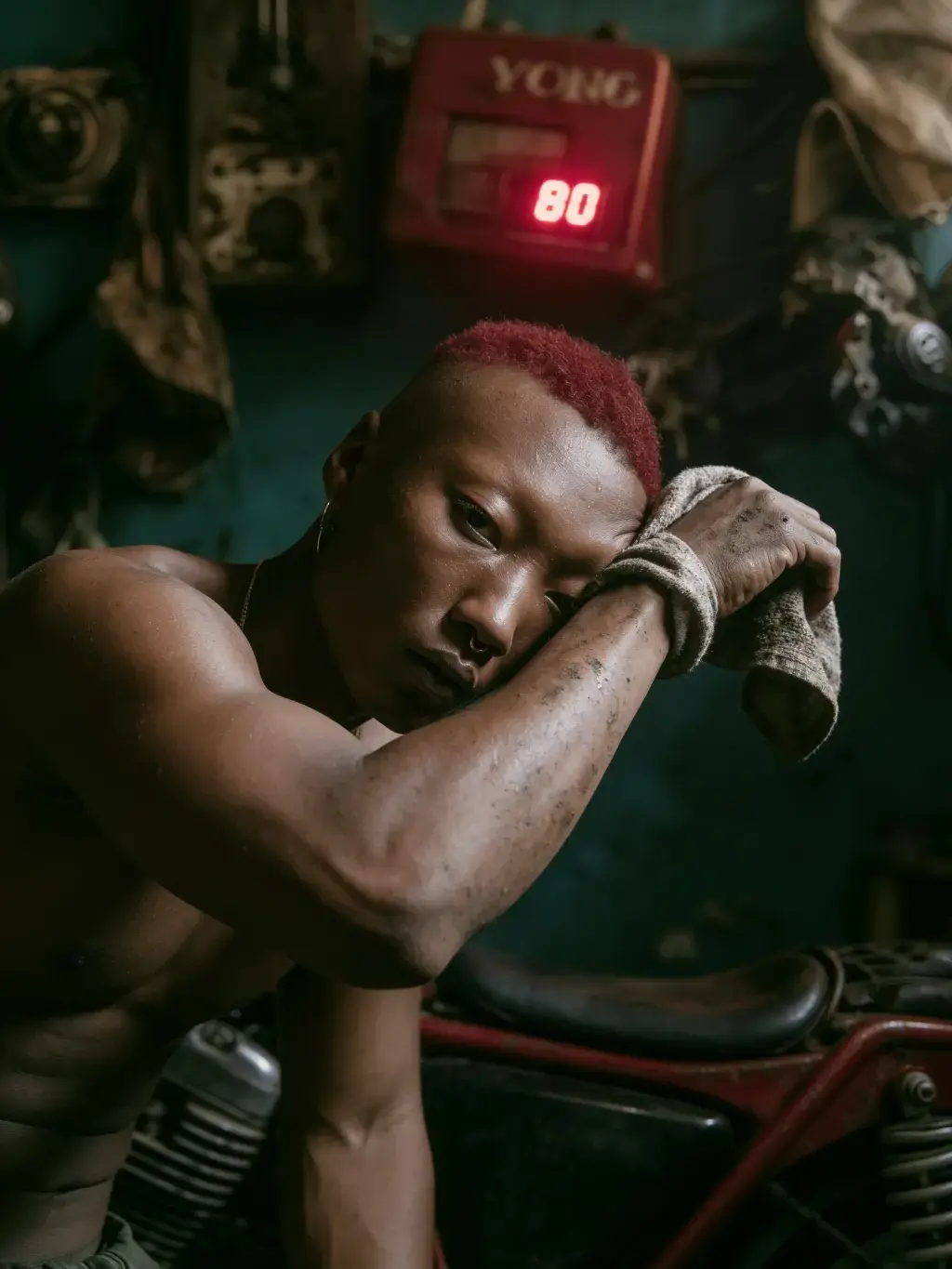 Homme torse nu aux cheveux rouges essuyant son visage avec un chiffon dans l'atelier YONG