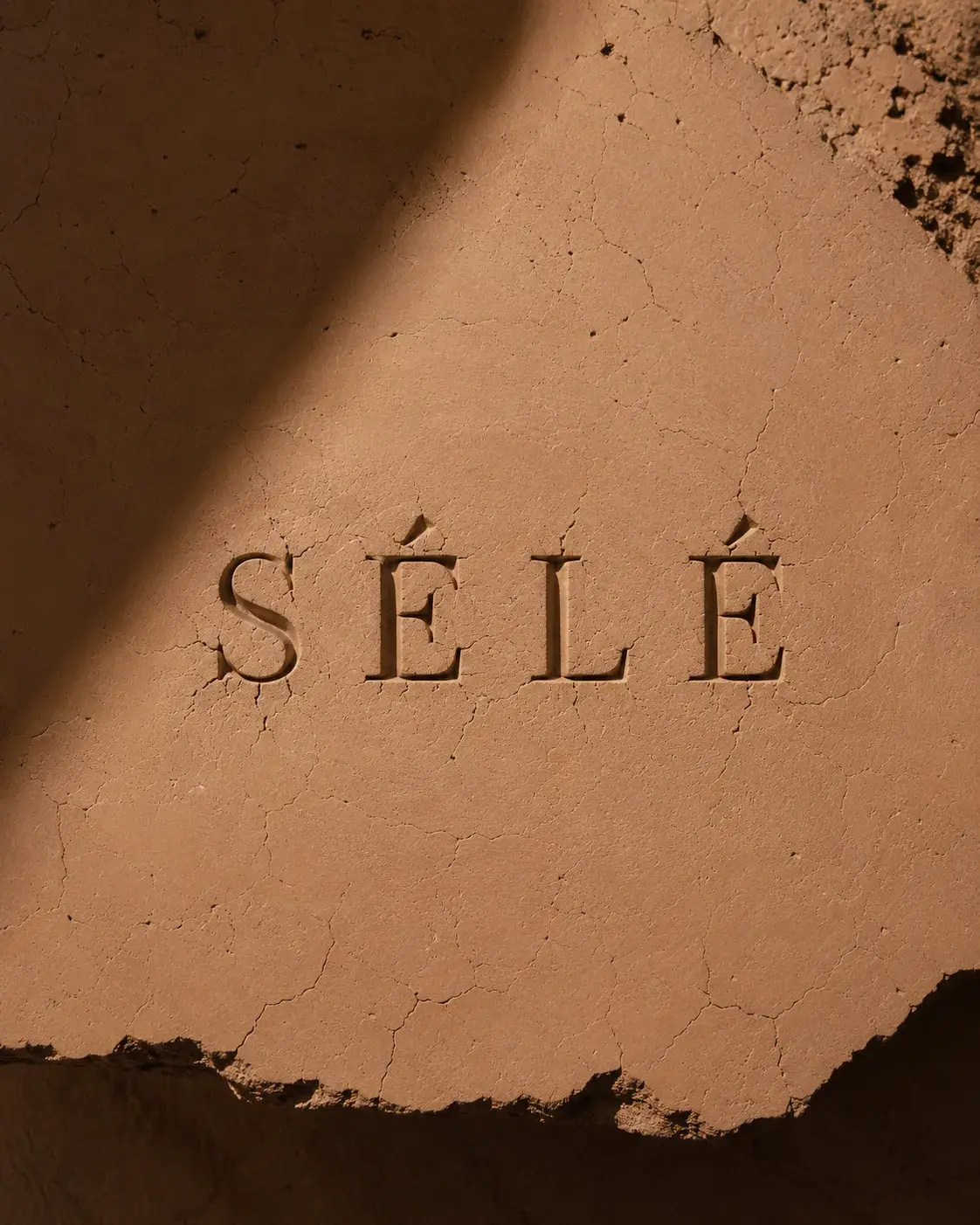 Inscription gravée dans mur de terre argile craquelée – ombre graphique, lumière sombre dramatique