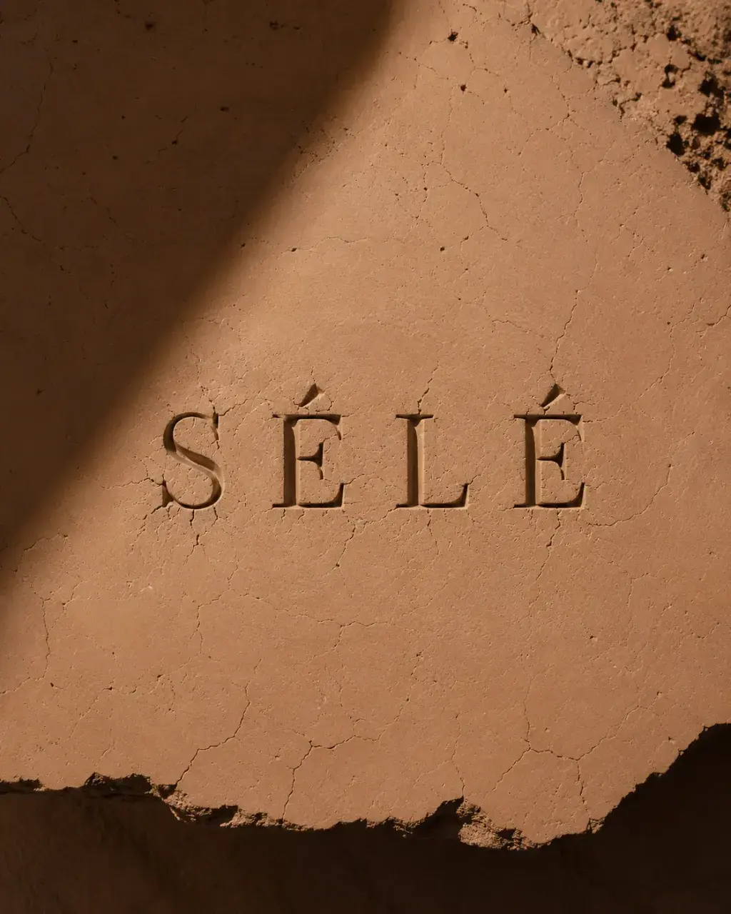 Inscription gravée dans mur de terre argile craquelée – ombre graphique, lumière sombre dramatique