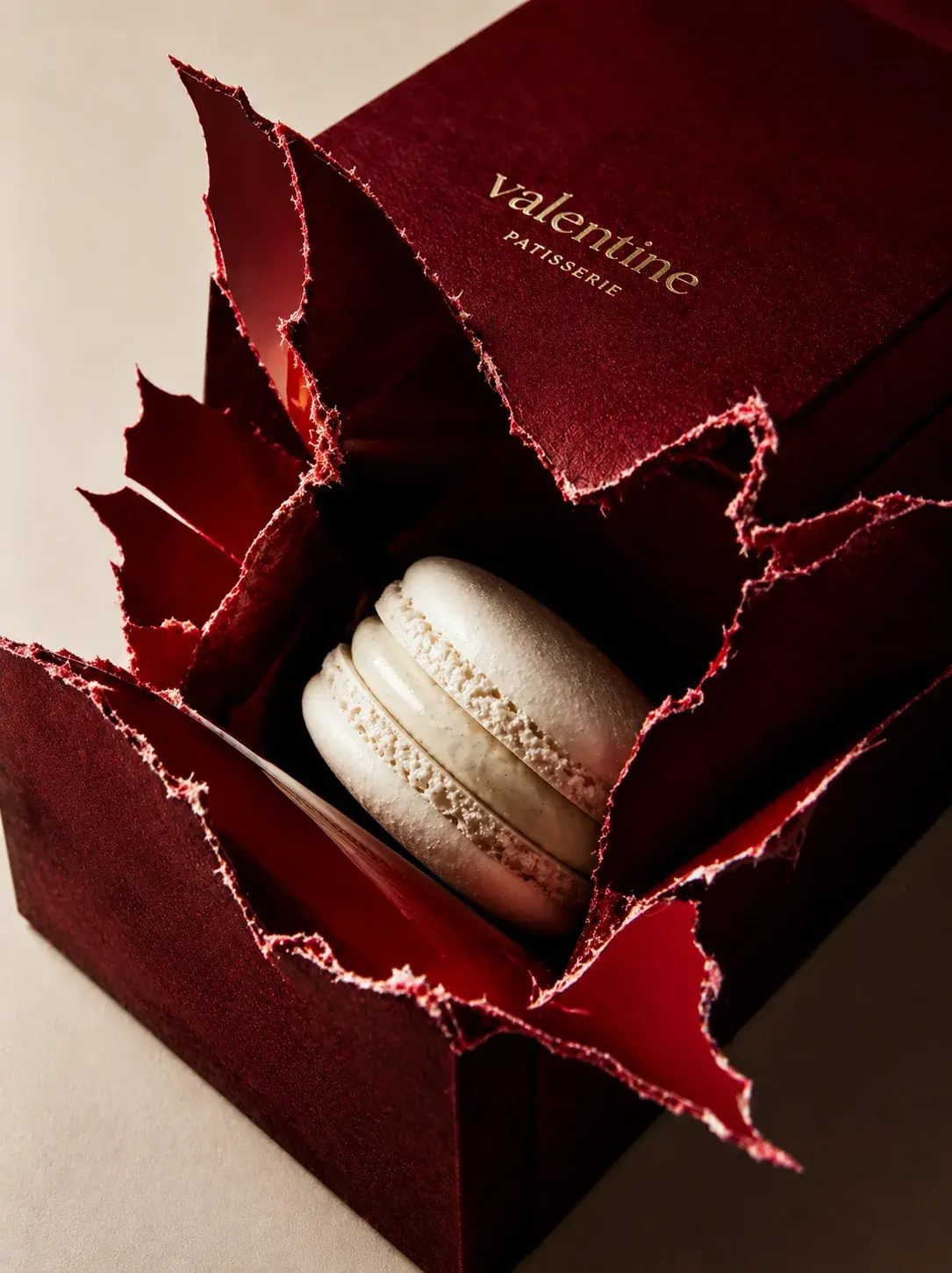 Macaron blanc dans boîte pâtisserie bordeaux éclatée – fond crème, packaging gastronomique