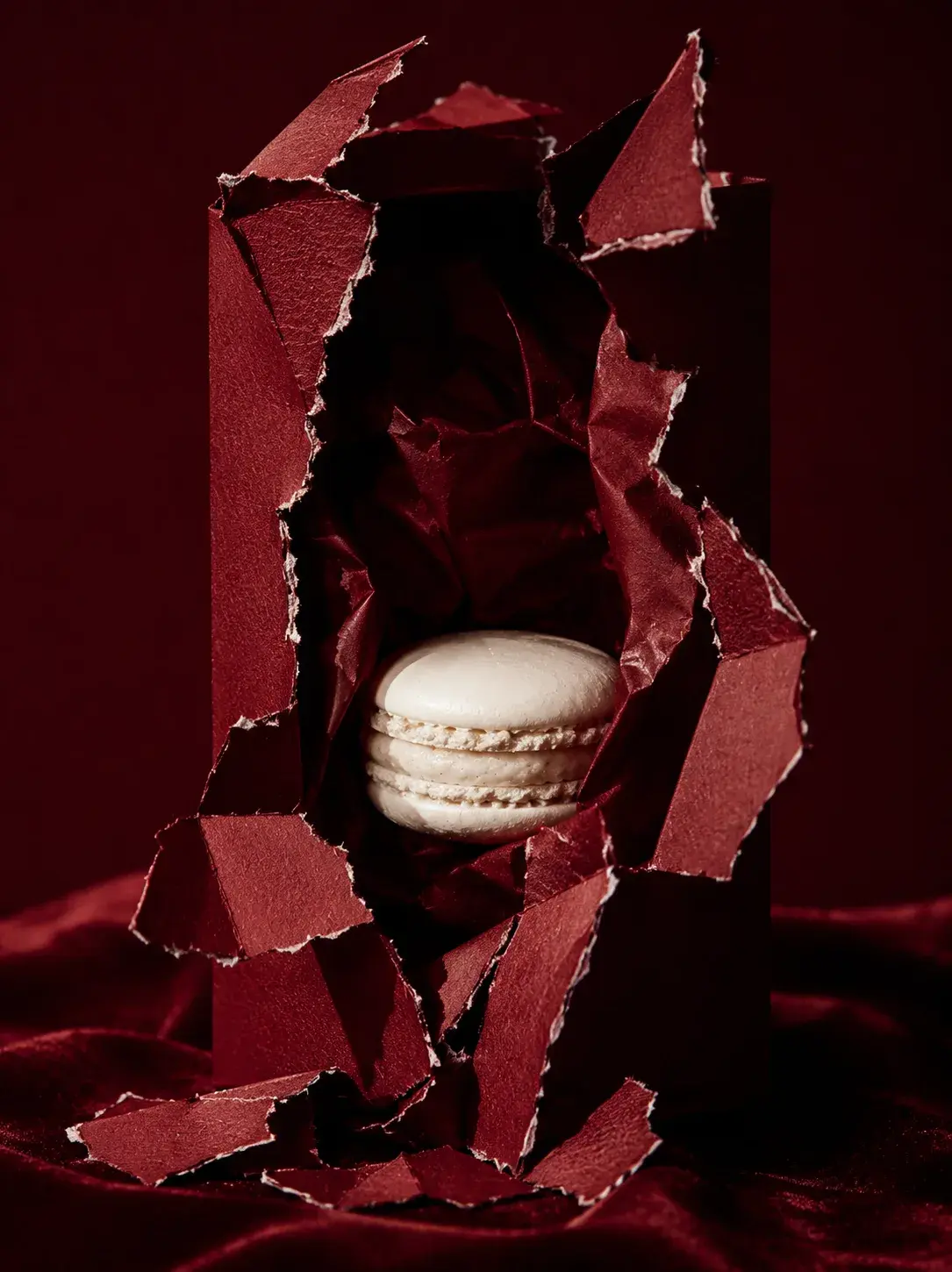Macaron blanc jaillissant d'une boîte pâtisserie bordeaux déchirée – fond velours, packaging