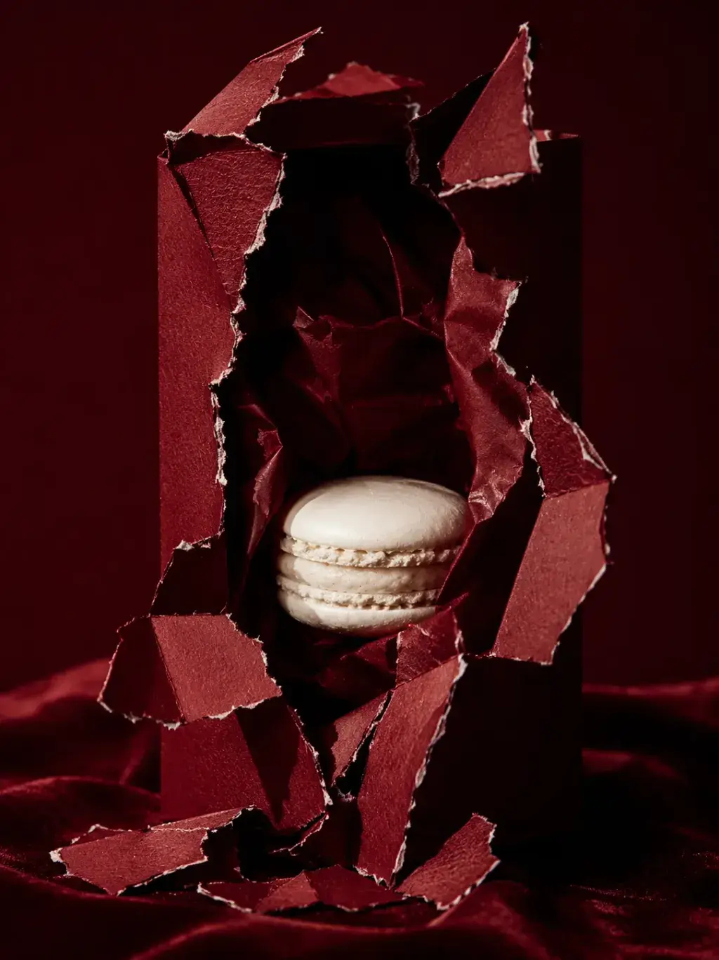 Macaron blanc jaillissant d'une boîte pâtisserie bordeaux déchirée – fond velours, packaging