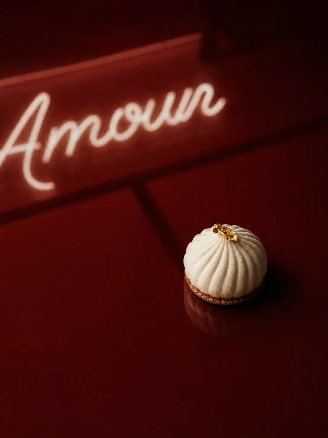 Macaron coquille cannelée blanche sur table bordeaux – enseigne néon diffus "Amour" en fond