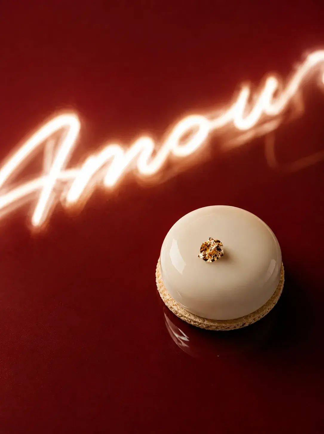 Macaron ivoire décoration or sur table bordeaux – enseigne néon calligraphie "Amour" en fond flou