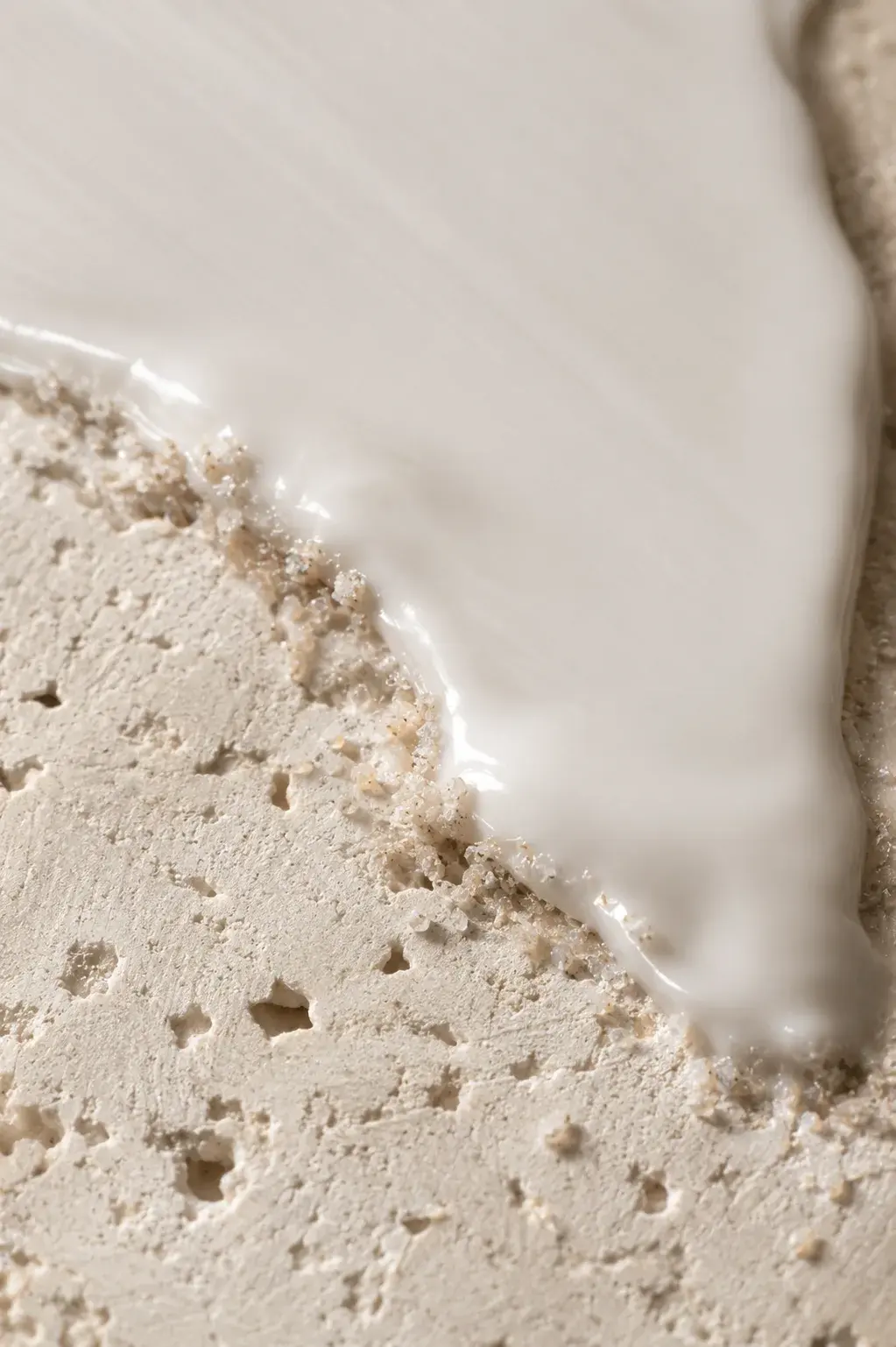 Macro crème blanche coulant sur bord de travertin poreux – contraste matières, fond neutre