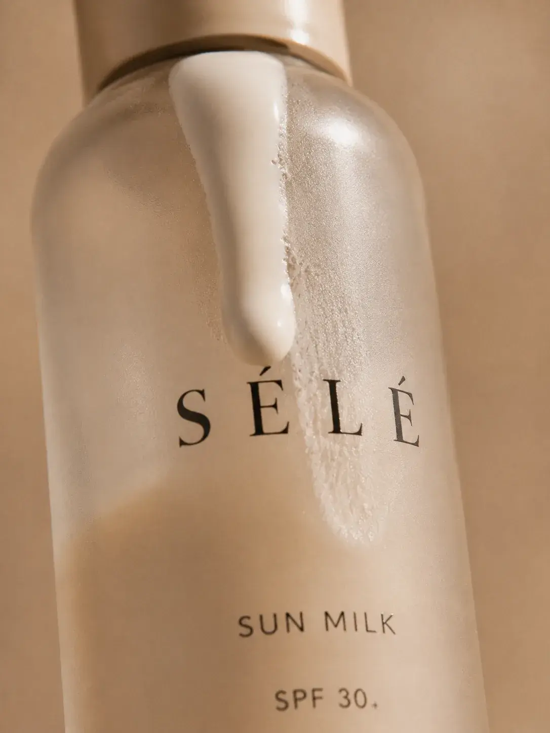 Macro flacon lait solaire verre – filet de lait blanc coulant, fond beige chaud, packaging luxe