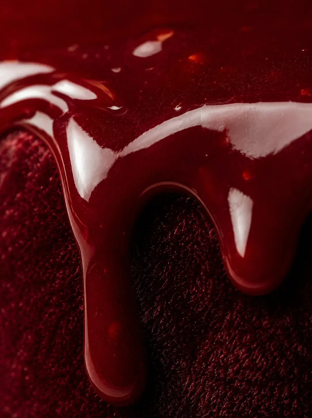Macro glaçage miroir bordeaux coulant sur velours rouge – reflets brillants, fond rouge profond