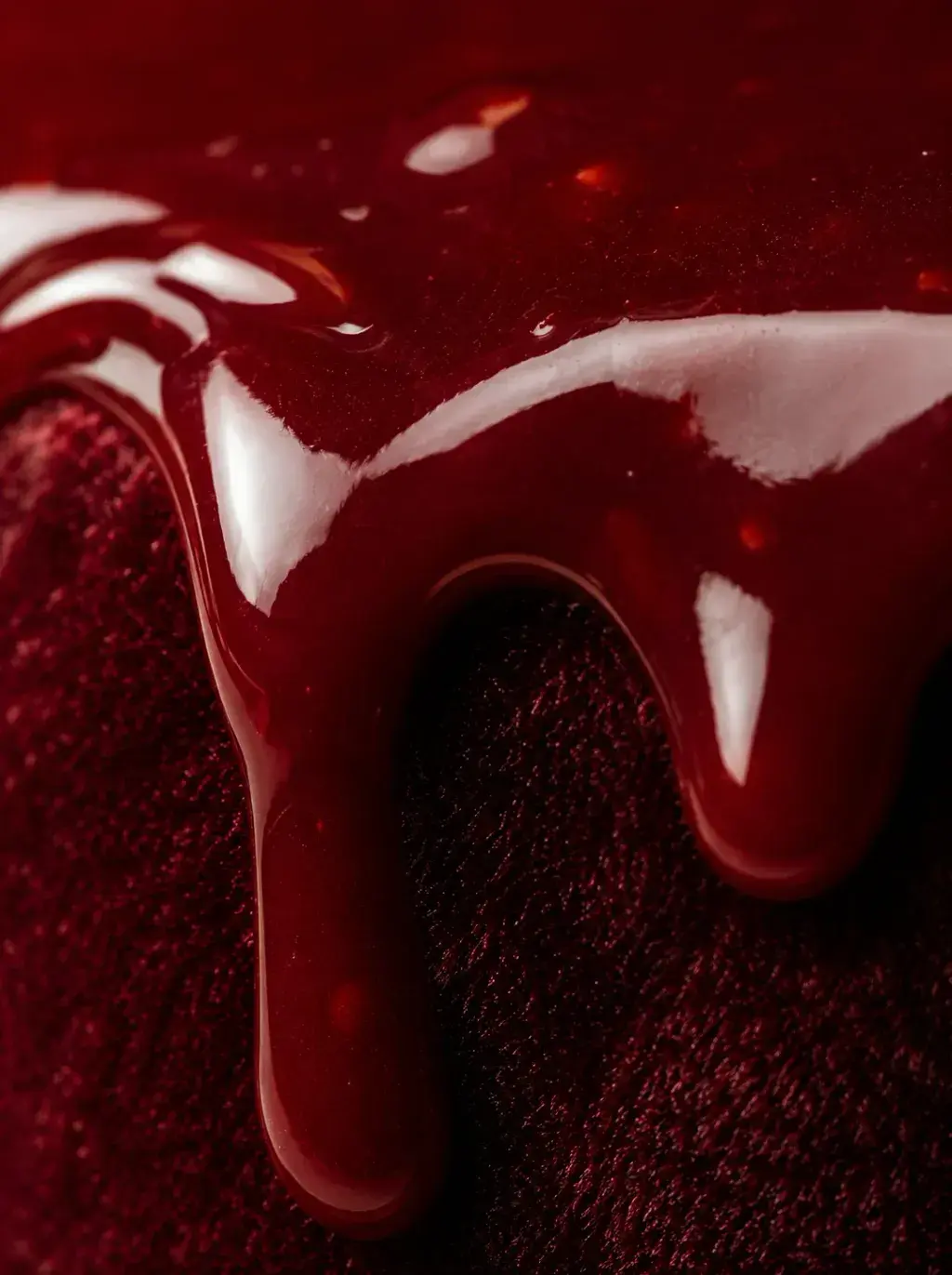 Macro glaçage miroir bordeaux coulant sur velours rouge – reflets brillants, fond rouge profond