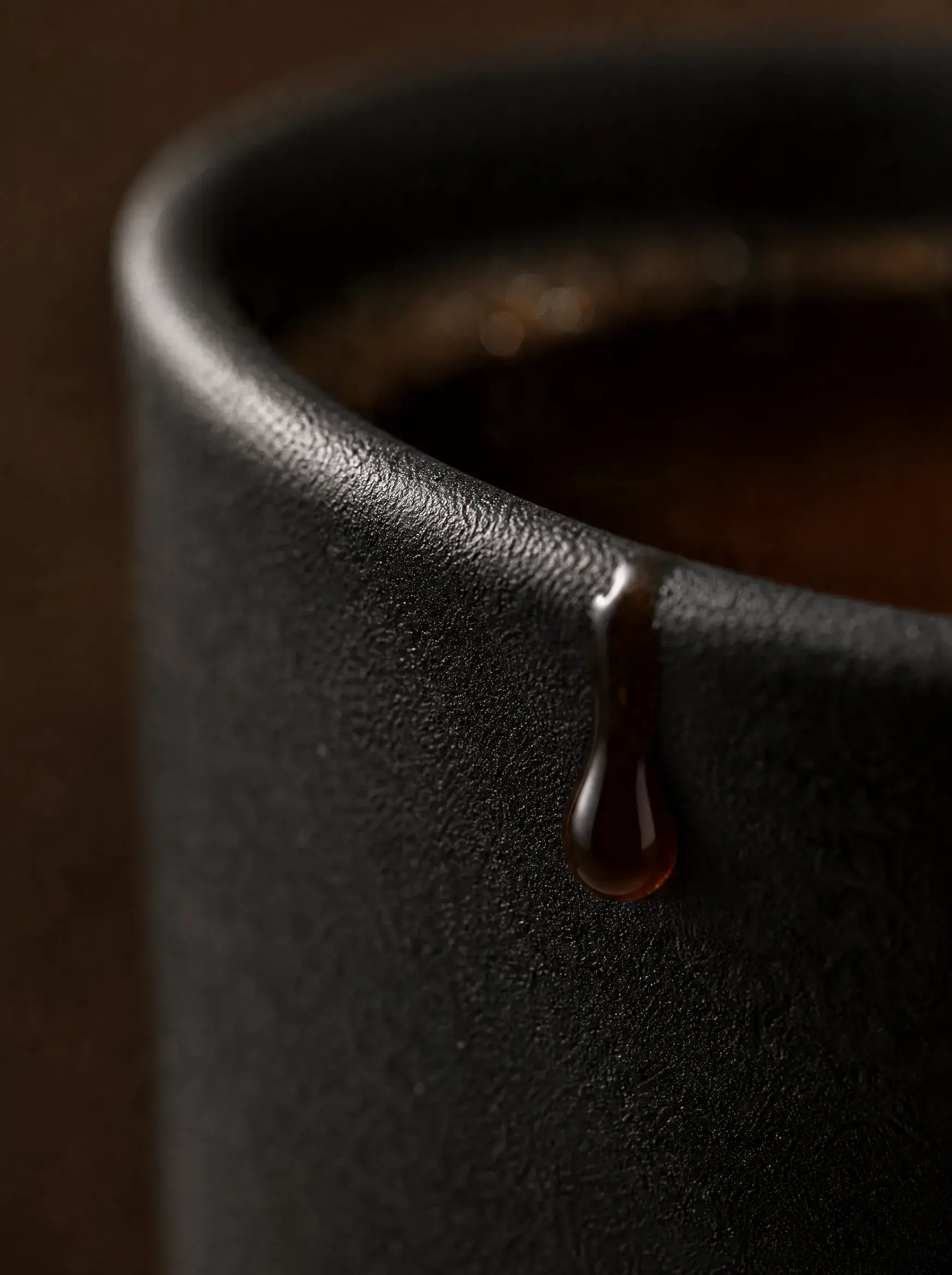 Macro – goutte de café coulant sur bord de tasse céramique noire, fond sombre brun