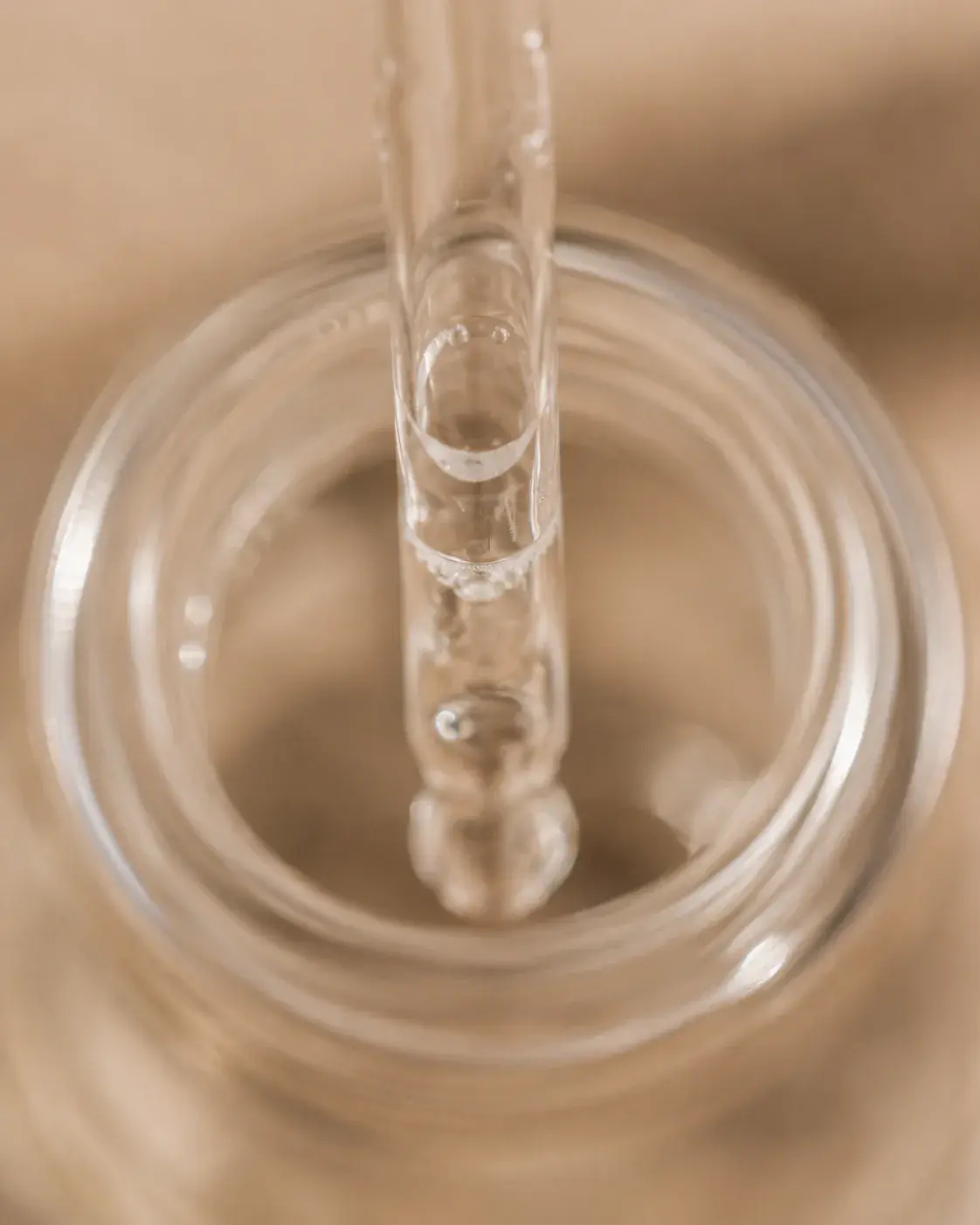 Macro pipette de verre plongeant dans flacon ouvert – bulles d'air, sérum translucide, fond beige