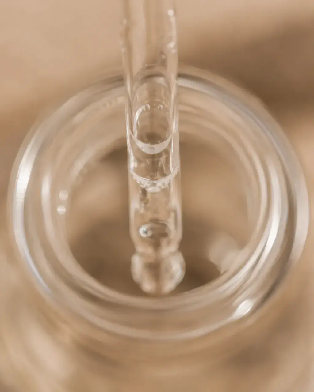 Macro pipette de verre plongeant dans flacon ouvert – bulles d'air, sérum translucide, fond beige
