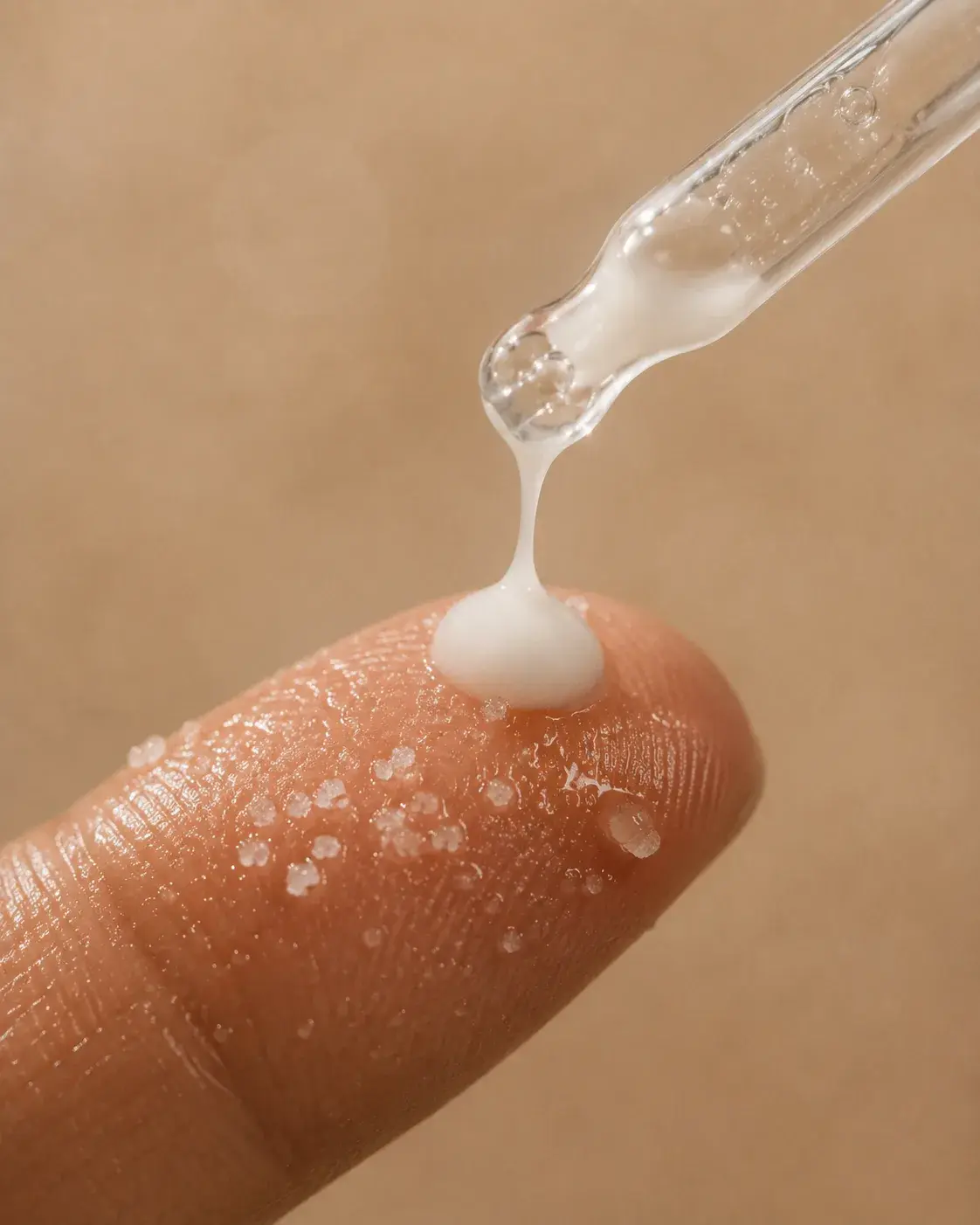 Macro pipette libérant du sérum sur le bout du doigt – gouttelettes sur peau, fond beige doux