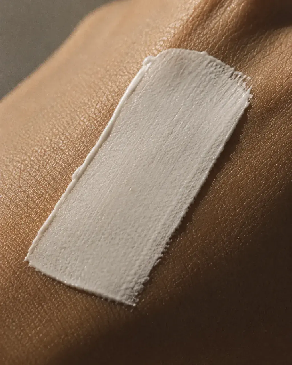 Macro swatch de crème solaire blanche appliquée sur peau foncée – test produit beauté