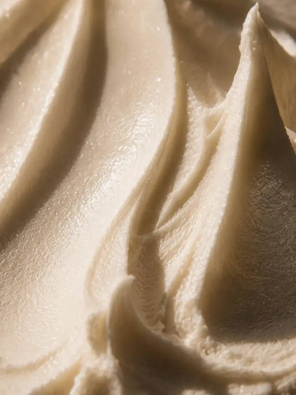 Macro texture crème beige dorée en pics et reliefs – surface onctueuse, lumière rasante dramatique