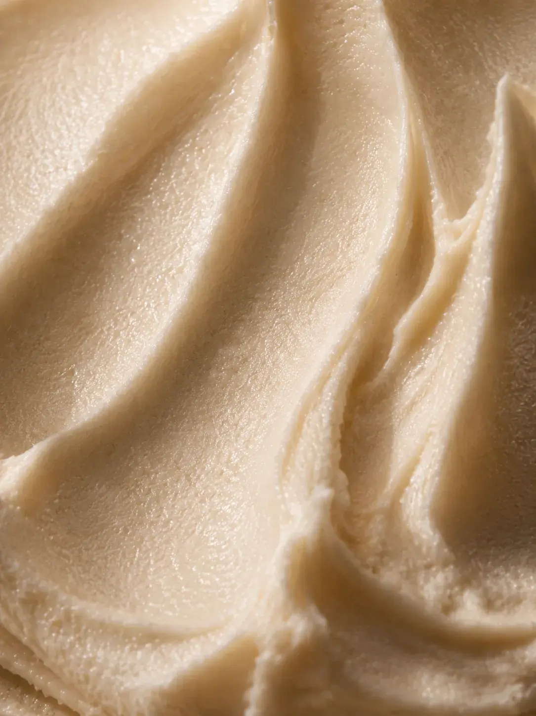 Macro texture crème beige en vagues et reliefs – formule riche, lumière rasante chaude