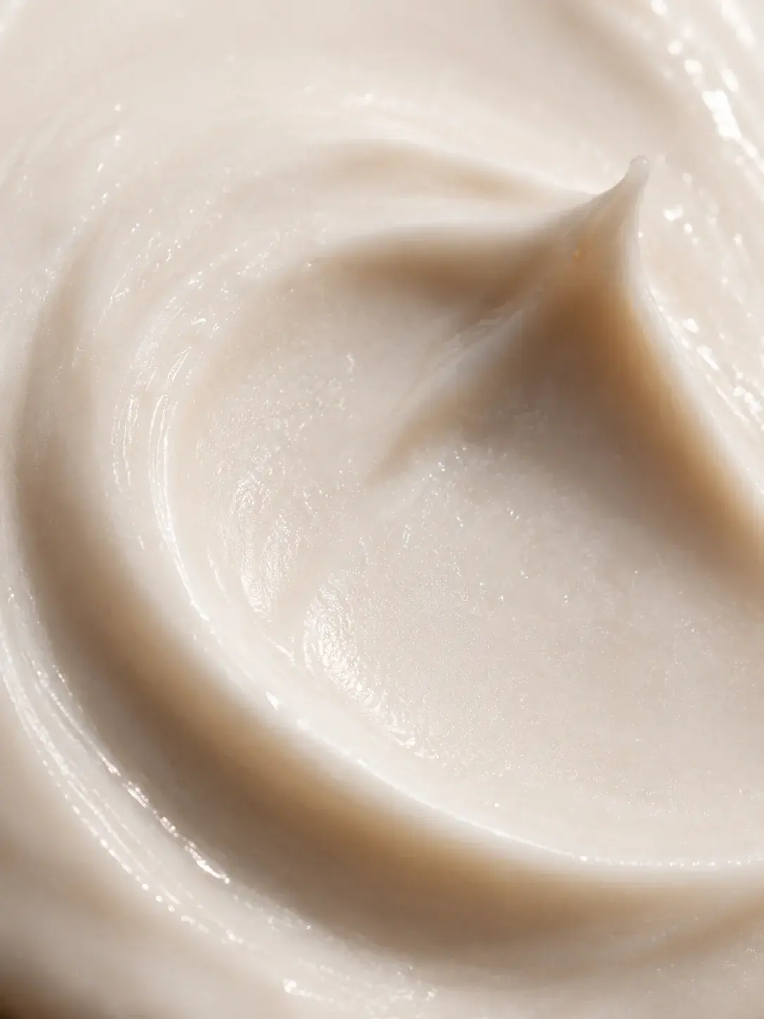 Macro très gros plan texture crème beige rosée en tourbillon – formule onctueuse, fond uni