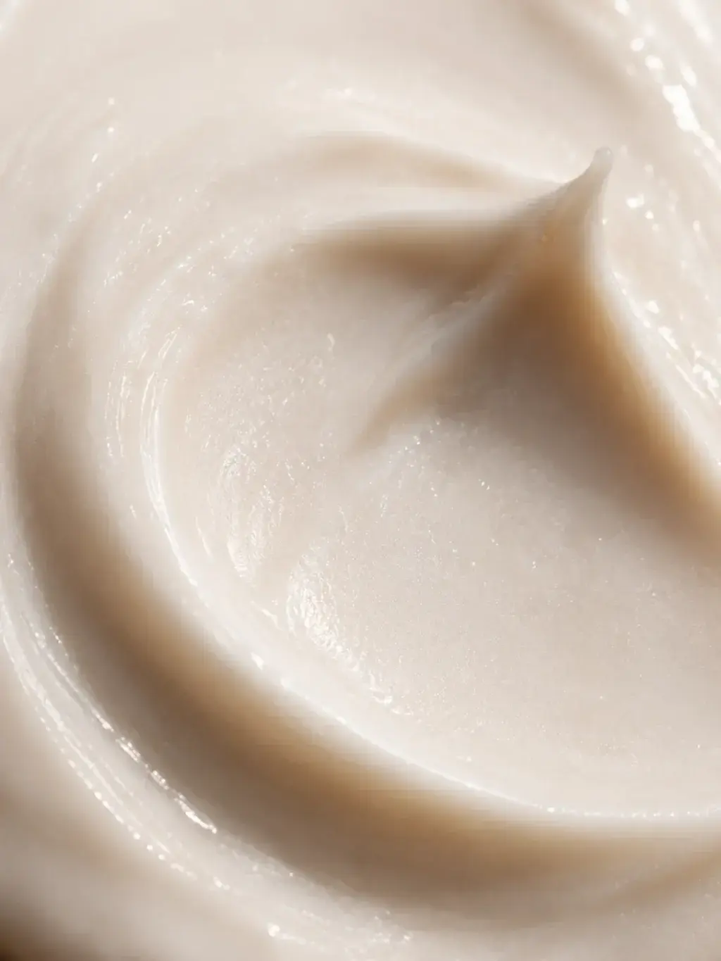 Macro très gros plan texture crème beige rosée en tourbillon – formule onctueuse, fond uni
