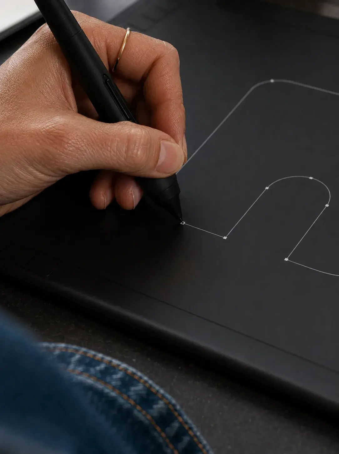 Main avec stylet traçant les courbes d'une lettre minuscule sur tablette graphique Wacom noire