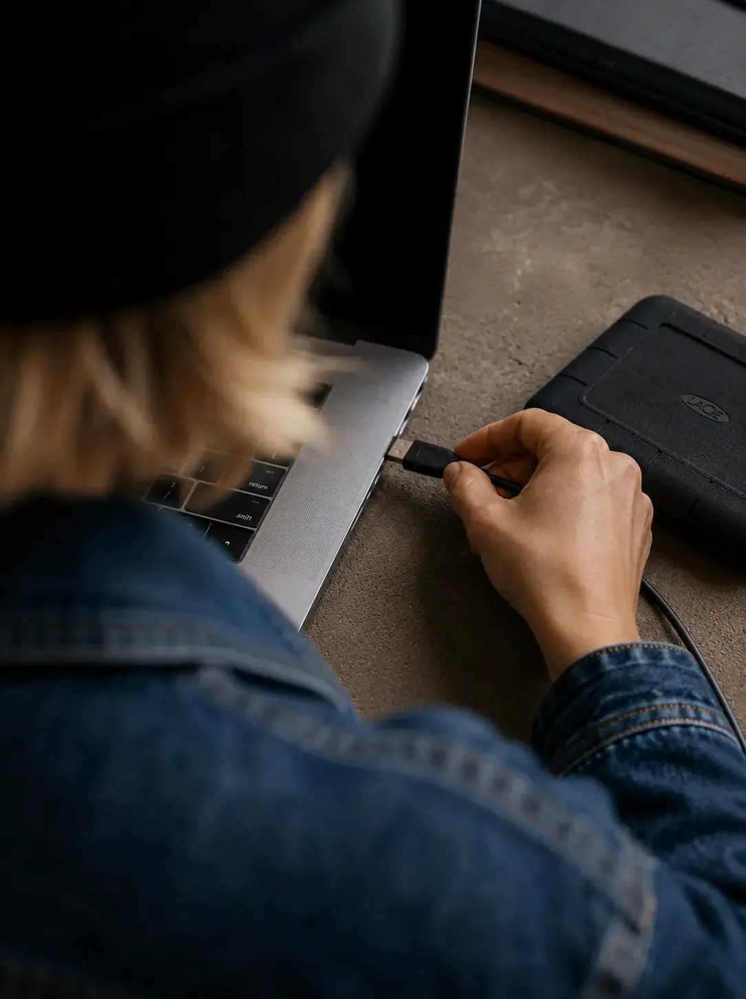 Main branchant une clé USB sur le port d'un laptop dans un bureau sombre avec disque dur externe à proximité
