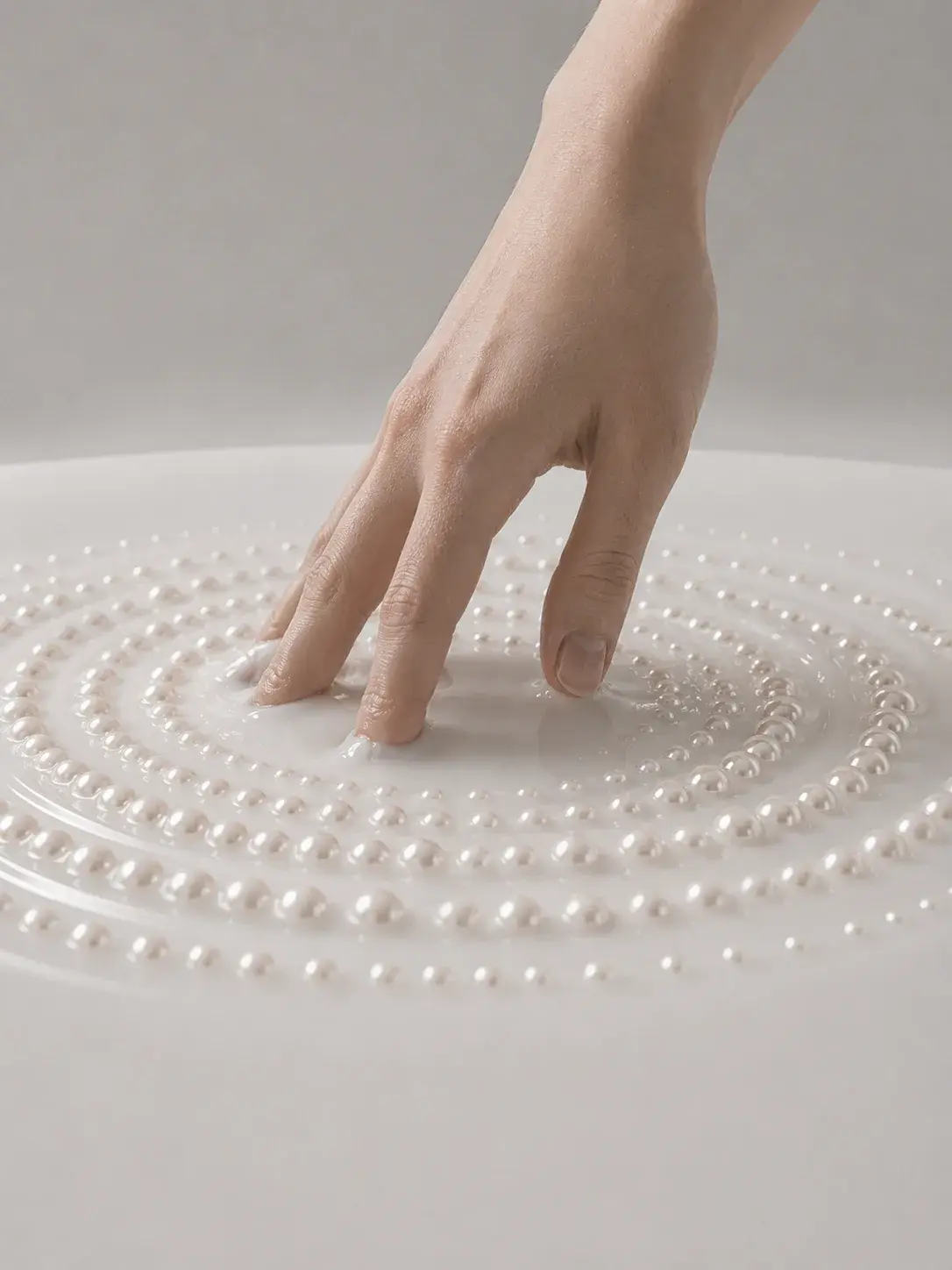 Main disposant des perles en spirale concentrique sur surface blanche, composition nacrée artisanale