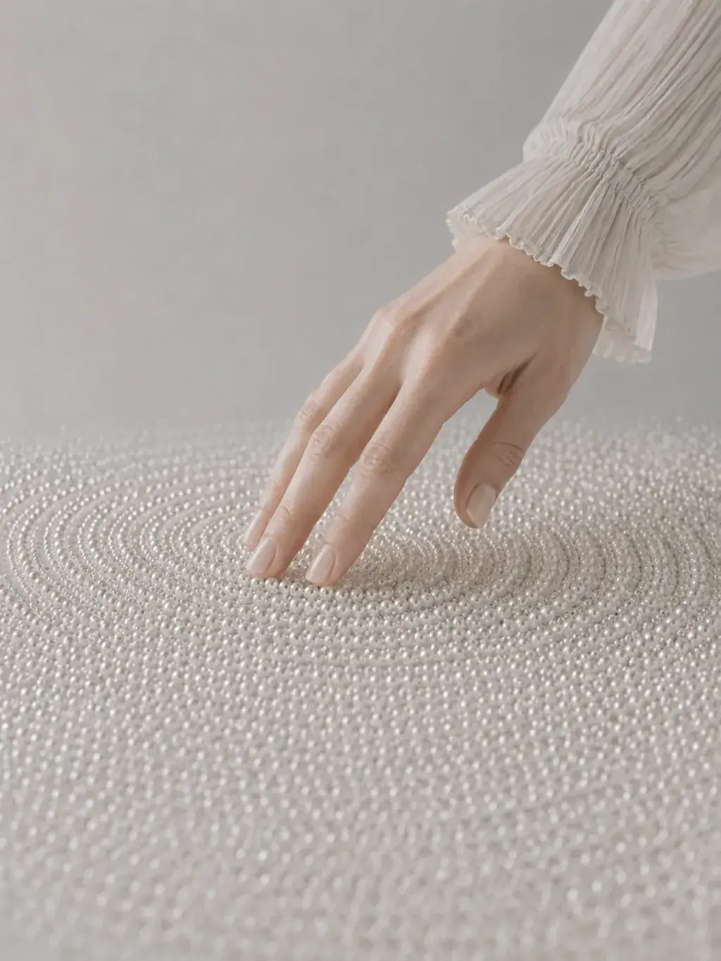 Main féminine en dentelle traçant des cercles dans un vaste tapis de micro-perles nacrées